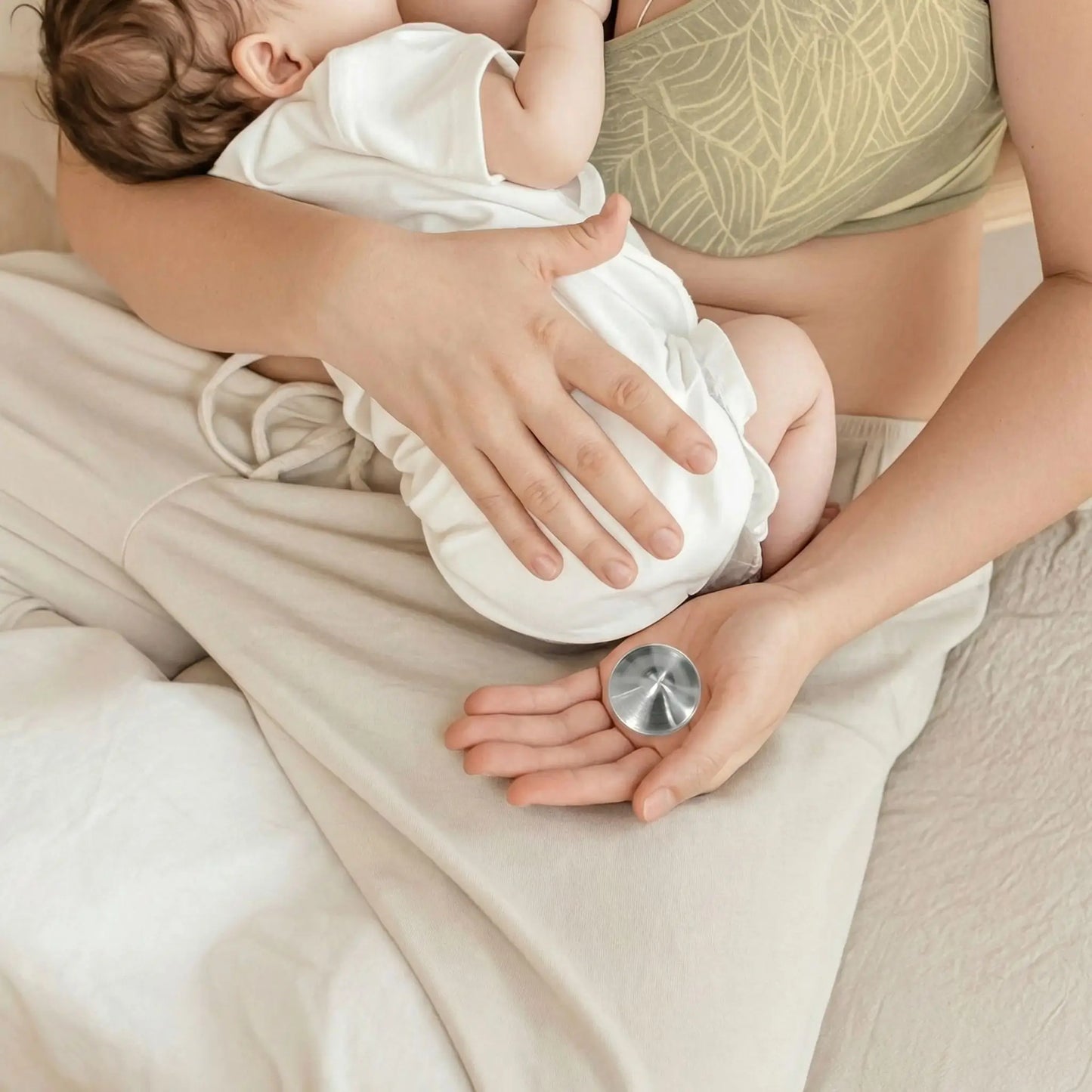 Coussinet d’allaitement en argent tri-laminé posé dans la main d’une maman pendant l’allaitement de son bébé