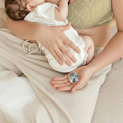 Coussinet d’allaitement en argent tri-laminé posé dans la main d’une maman pendant l’allaitement de son bébé