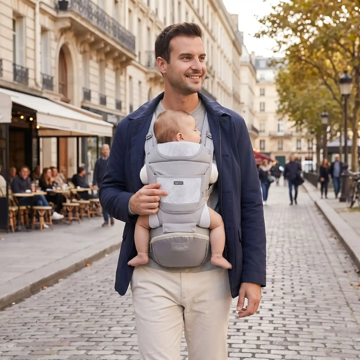AËL Porte bébé hip seat lifestyle - Papa portant bébé dans les rues pavées de Paris, coloris Gris Perle